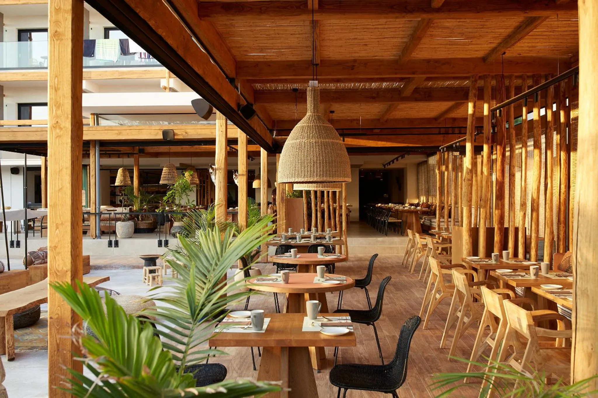 Une salle à manger lumineuse avec des tables en bois et des suspensions en fibres naturelles.
