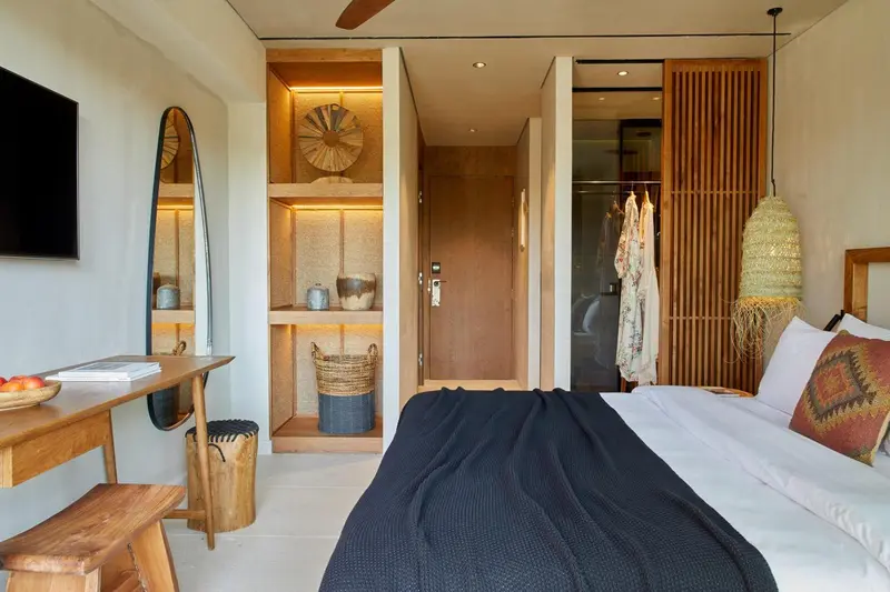 Une chambre lumineuse avec un lit recouvert d'une couverture sombre et un espace de rangement ouvert.