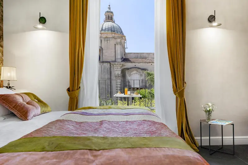 Une chambre avec un lit recouvert d'une courtepointe colorée offre une vue sur un bâtiment historique.