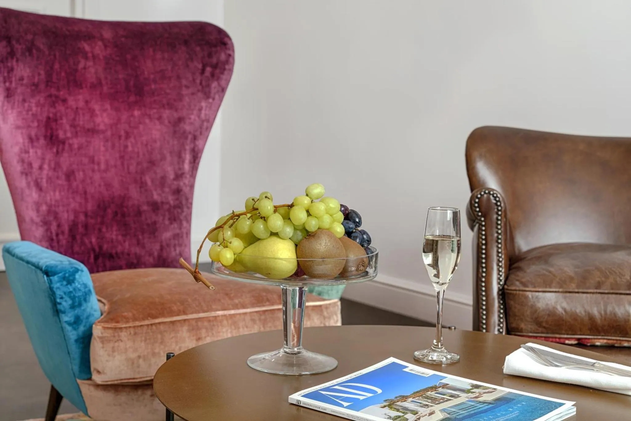 Nature morte avec un verre de champagne, des fruits et des magazines sur une table basse.