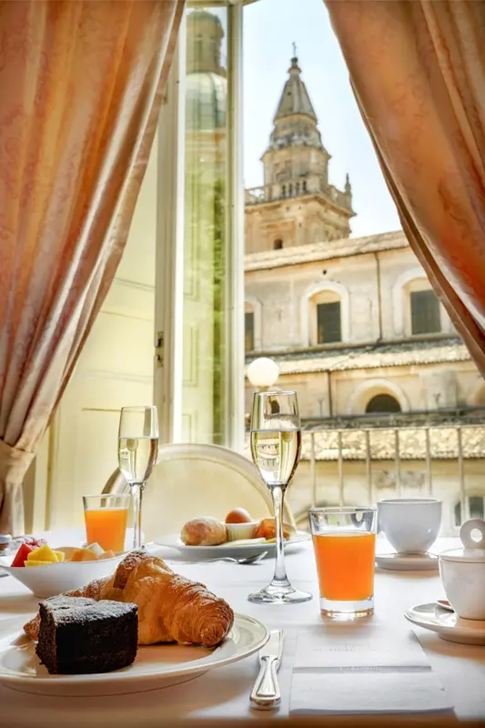 Une table est dressée avec un petit-déjeuner devant une fenêtre ouverte sur une vue urbaine.