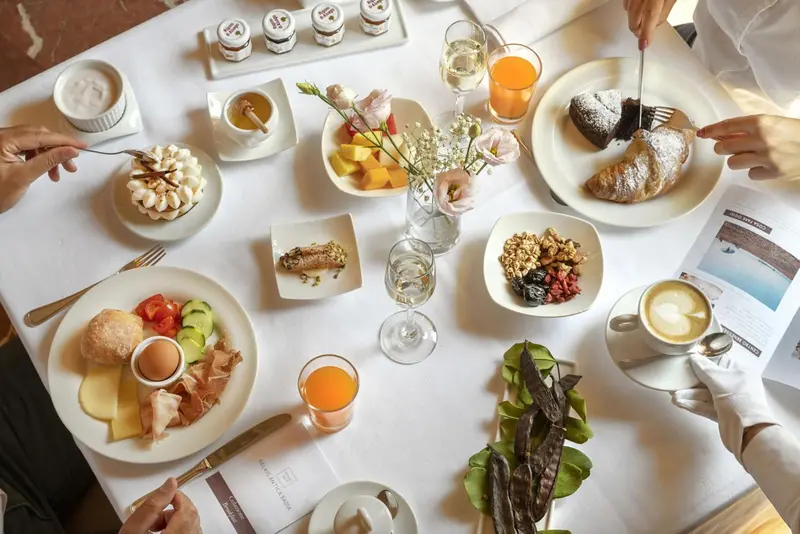 Une table est dressée pour un petit-déjeuner avec des viennoiseries, des fruits et des boissons.