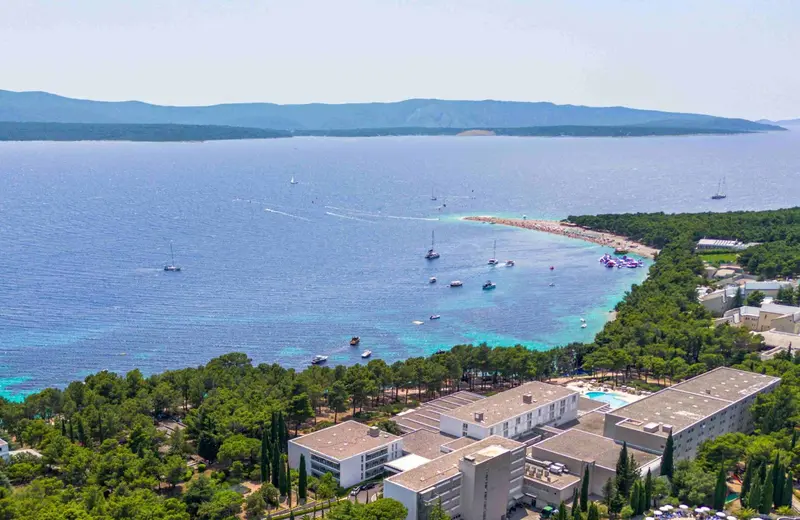Vue aérienne d'un complexe hôtelier blanc surplombant une crique turquoise.