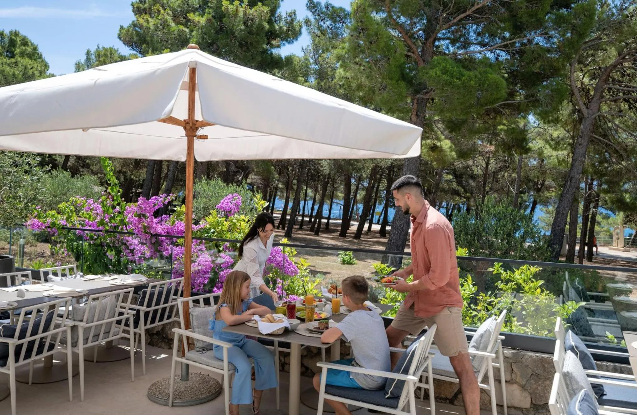 Une famille prend son petit-déjeuner sur une terrasse ensoleillée avec vue sur la mer.