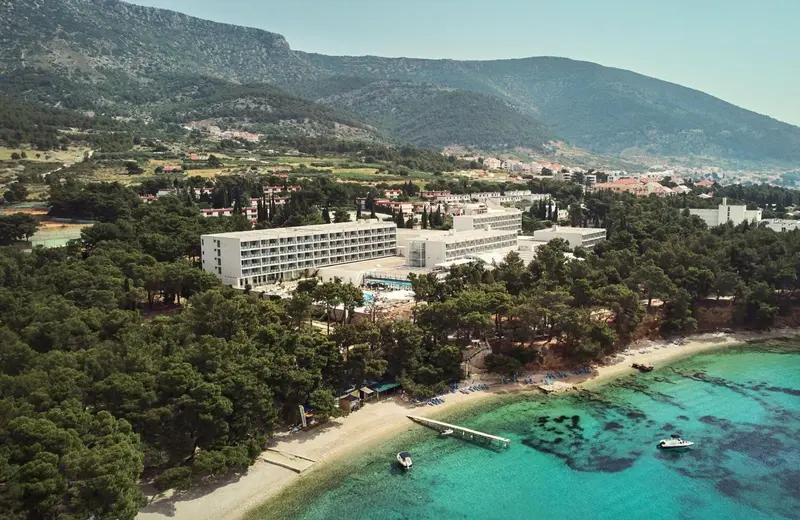 Vue aérienne d'un complexe hôtelier blanc bordant une plage de sable et une mer turquoise.