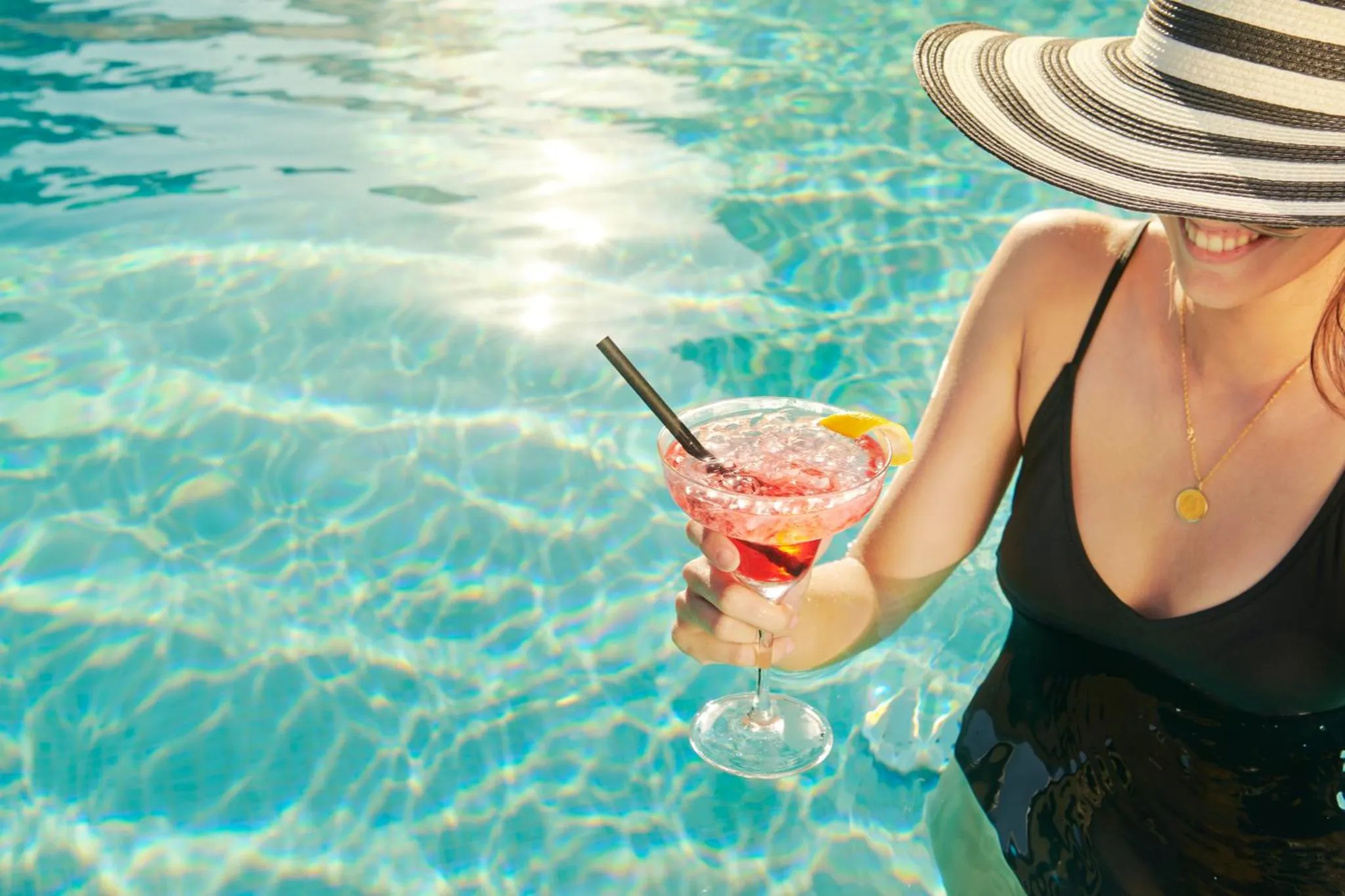 Une personne déguste une boisson rafraîchissante au bord d'une piscine ensoleillée.