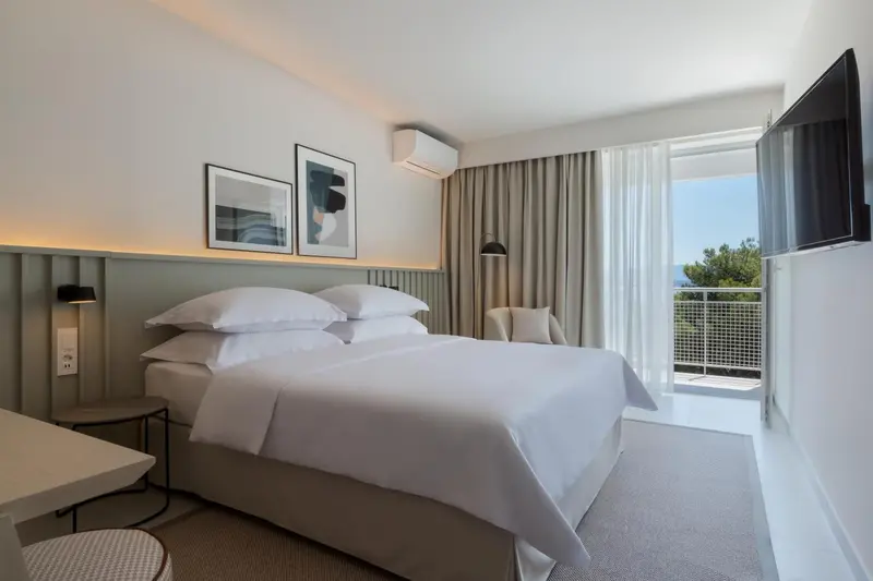 Une chambre lumineuse avec un grand lit et un accès à un balcon.