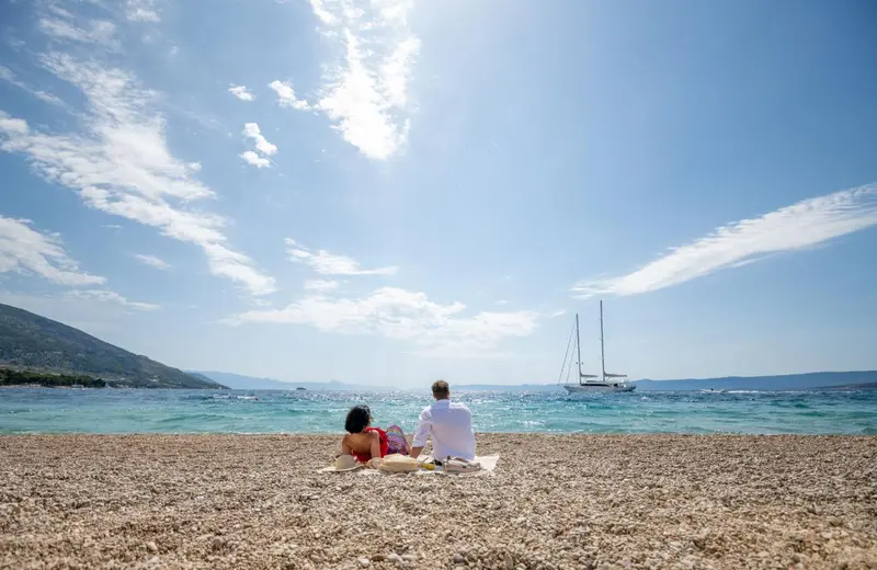 Deux personnes sont assises sur une plage de galets face à la mer.