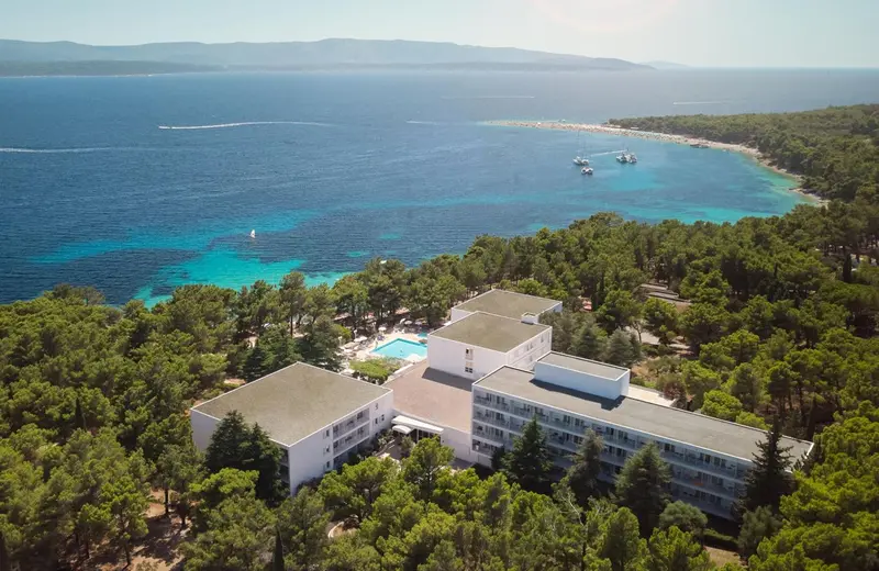 Vue aérienne d'un bâtiment blanc au milieu d'une végétation luxuriante, surplombant une crique turquoise.