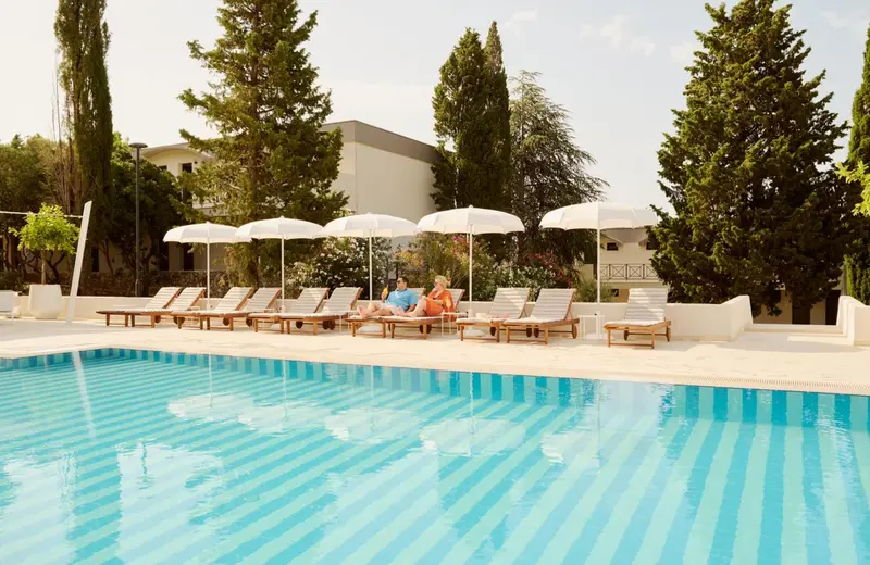 Transats blancs disposés au bord d'une piscine turquoise sous des parasols.