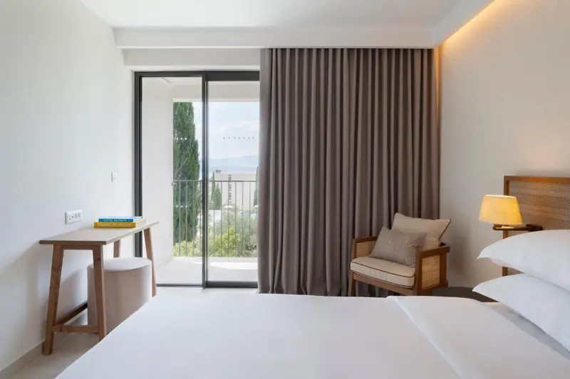 Chambre lumineuse avec un bureau et un fauteuil près d'une grande baie vitrée.