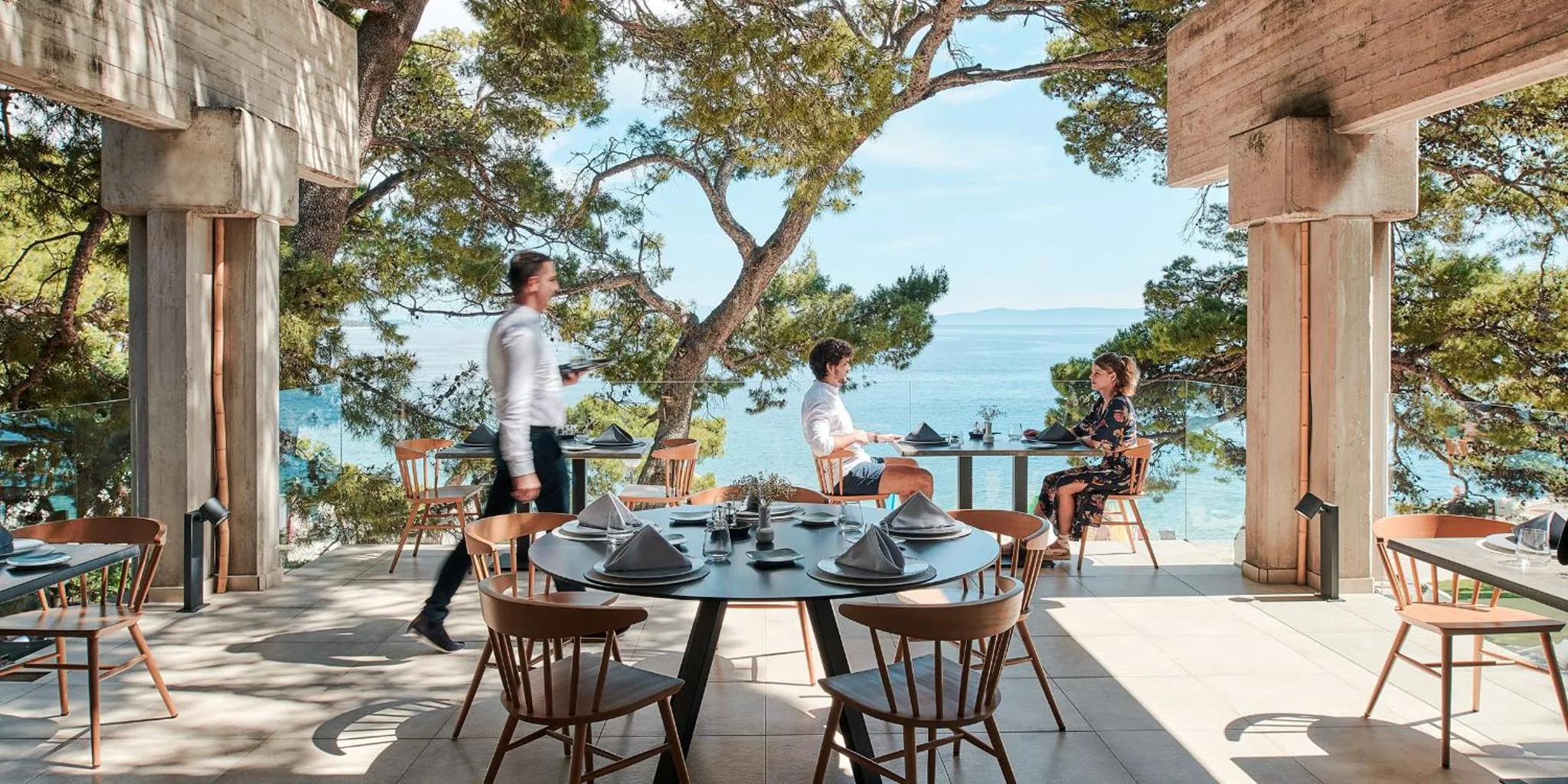 Une terrasse ombragée avec des tables dressées face à la mer.