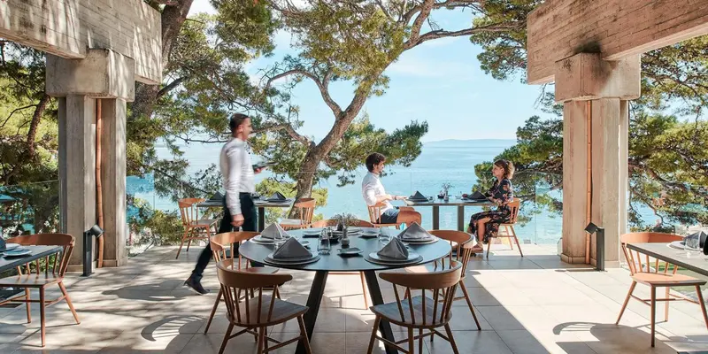 Une terrasse ombragée avec des tables dressées face à la mer.