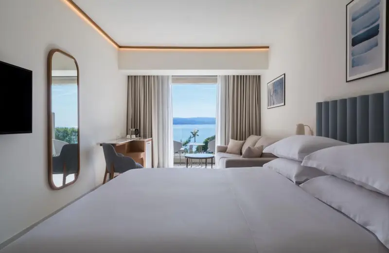 Chambre lumineuse avec un lit confortable et un coin salon donnant sur la mer.