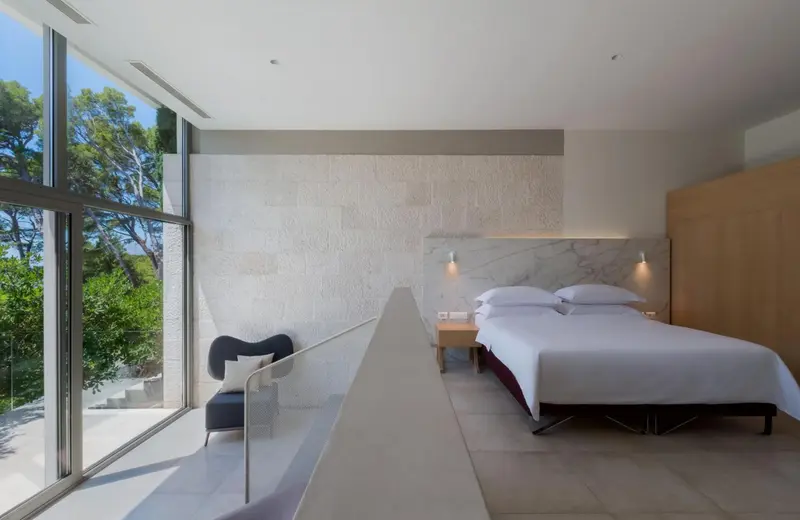 Une chambre lumineuse avec un grand lit et un coin salon donnant sur un jardin.