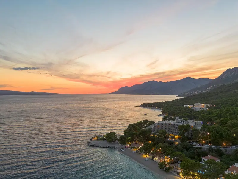 Vue aérienne d'une côte rocheuse au coucher du soleil, avec des bâtiments et une plage.