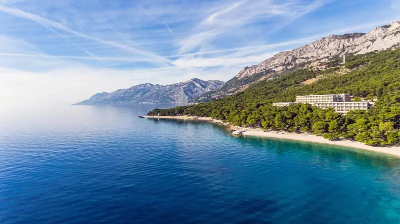 Vue aérienne d'un bâtiment blanc le long d'une côte rocheuse et d'une plage de sable.