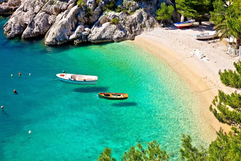 Une plage de sable fin bordée d'une eau turquoise et de rochers.