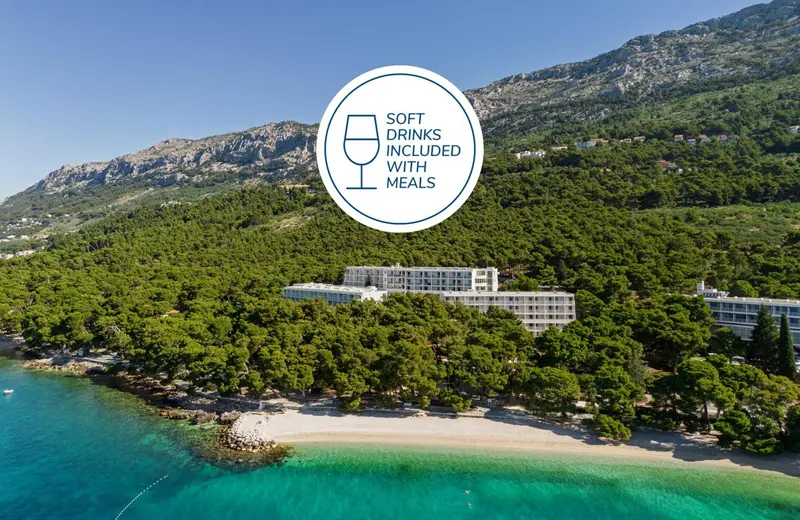 Vue aérienne d'un bâtiment blanc entouré de végétation et bordant une plage de sable fin.