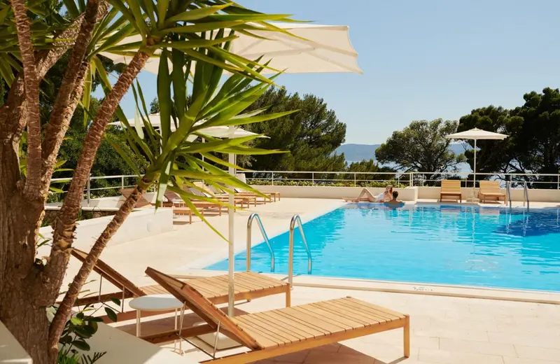 Transats et parasols bordent une piscine rectangulaire turquoise.