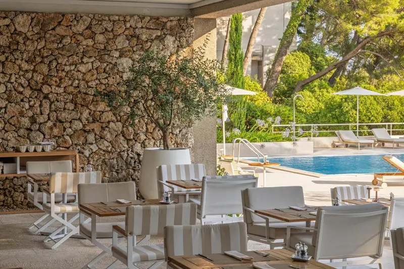 Tables et chaises blanches dressées sur une terrasse ombragée près d'une piscine.