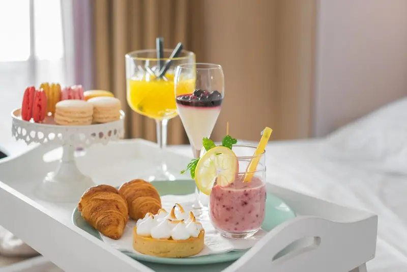 Un plateau de petit-déjeuner avec des pâtisseries et des boissons fraîches est présenté sur un lit.