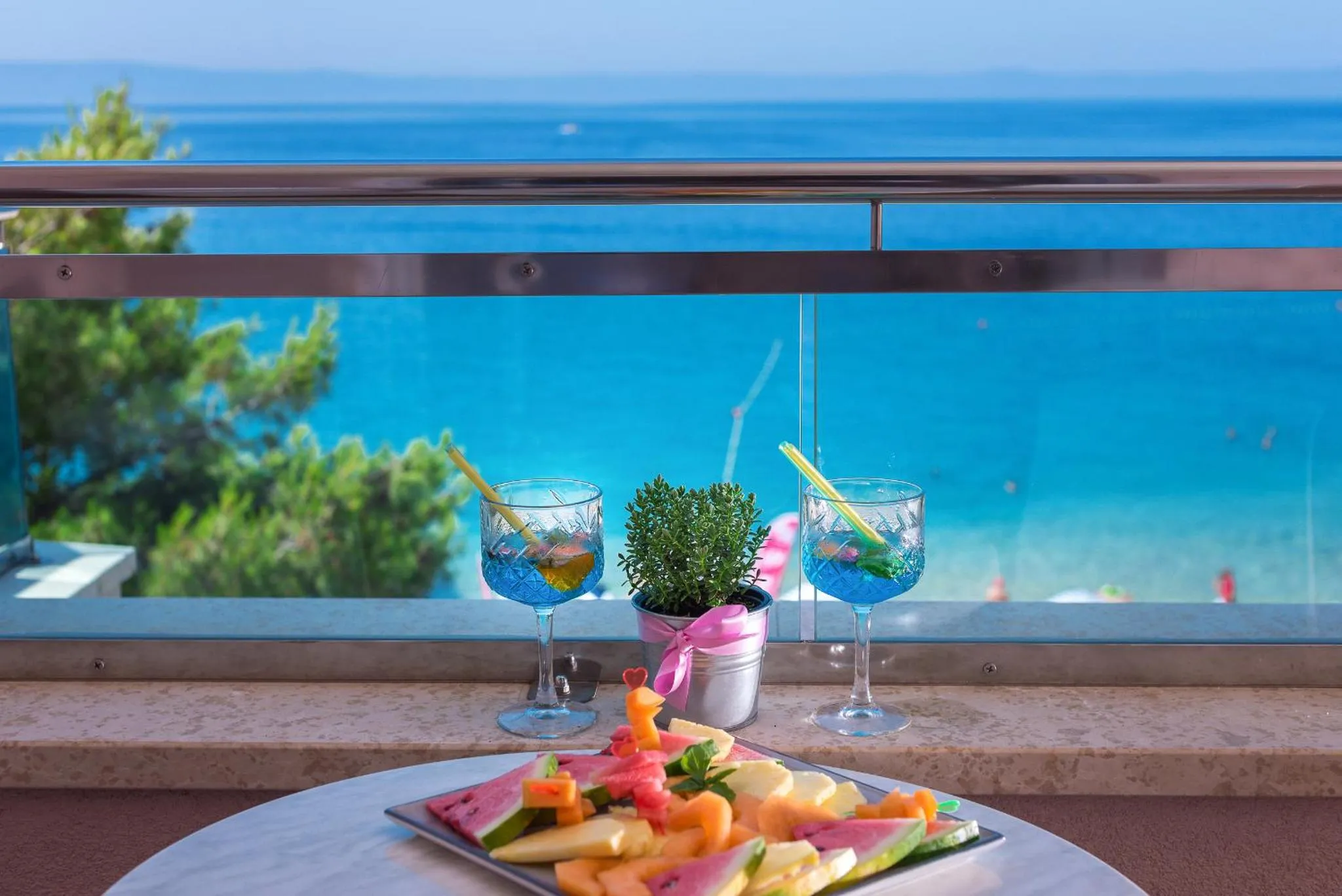 Une table ronde avec des fruits frais et des boissons sur une terrasse ensoleillée avec vue sur la mer.