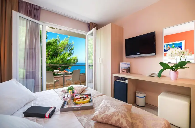 Chambre lumineuse avec un lit preparé et une vue sur la mer depuis un balcon.