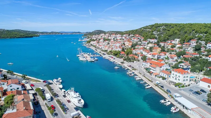Vue aérienne d'une ville côtière avec un port de plaisance et des bâtiments aux toits rouges.