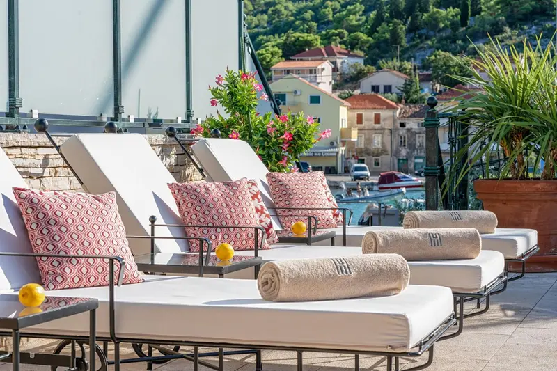 Transats blancs avec coussins rouges et serviettes enroulées sur une terrasse ensoleillée.