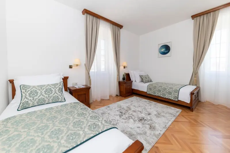 Chambre lumineuse avec deux lits simples et un tapis au sol.