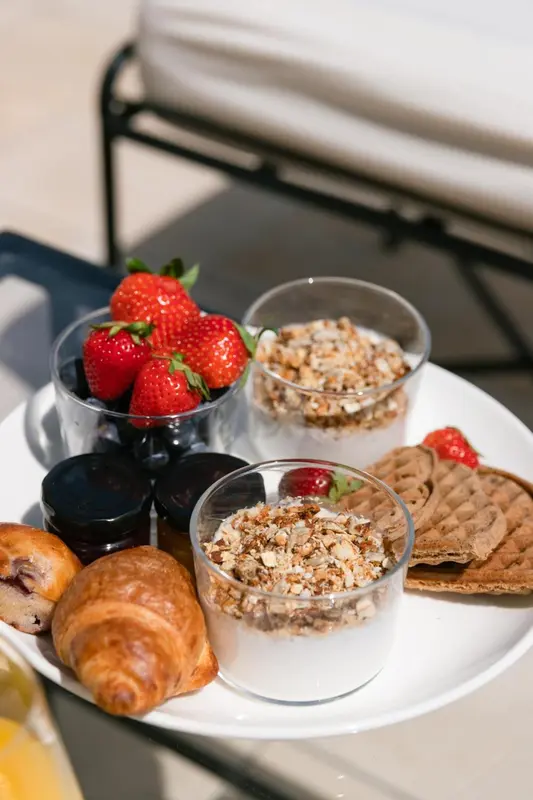 Un petit-déjeuner avec des fruits frais, des viennoiseries et des yaourts est présenté sur une table.
