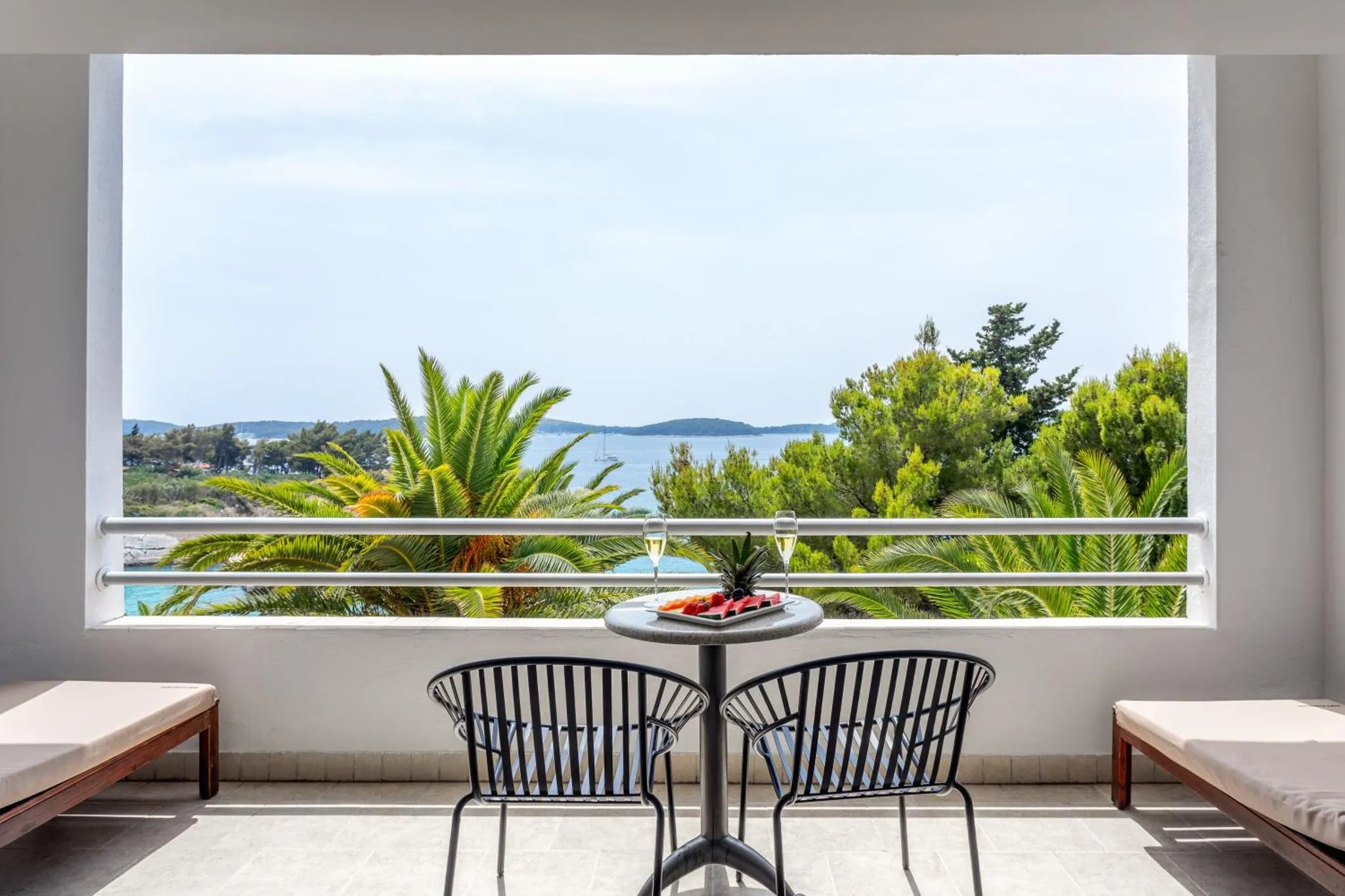 Une terrasse avec une table basse et deux fauteuils offre une vue sur la mer et la végétation.