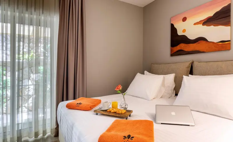 Une chambre lumineuse avec un lit recouvert d'une couverture orange et d'un plateau de petit-déjeuner.