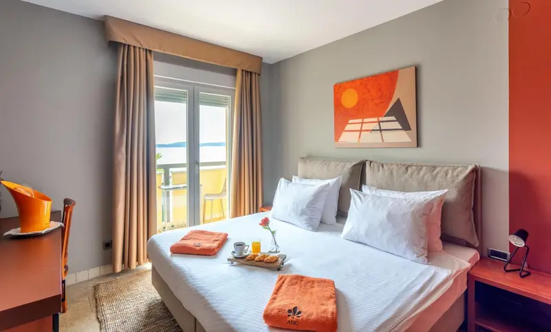Une chambre lumineuse avec un grand lit et un balcon donnant sur la mer.