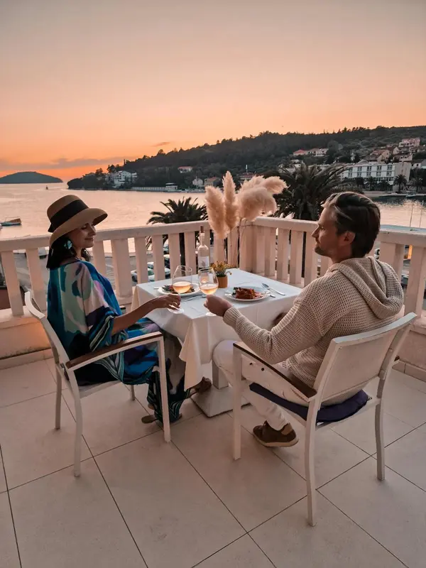 Un couple est assis à une table en extérieur face à la mer au coucher du soleil.