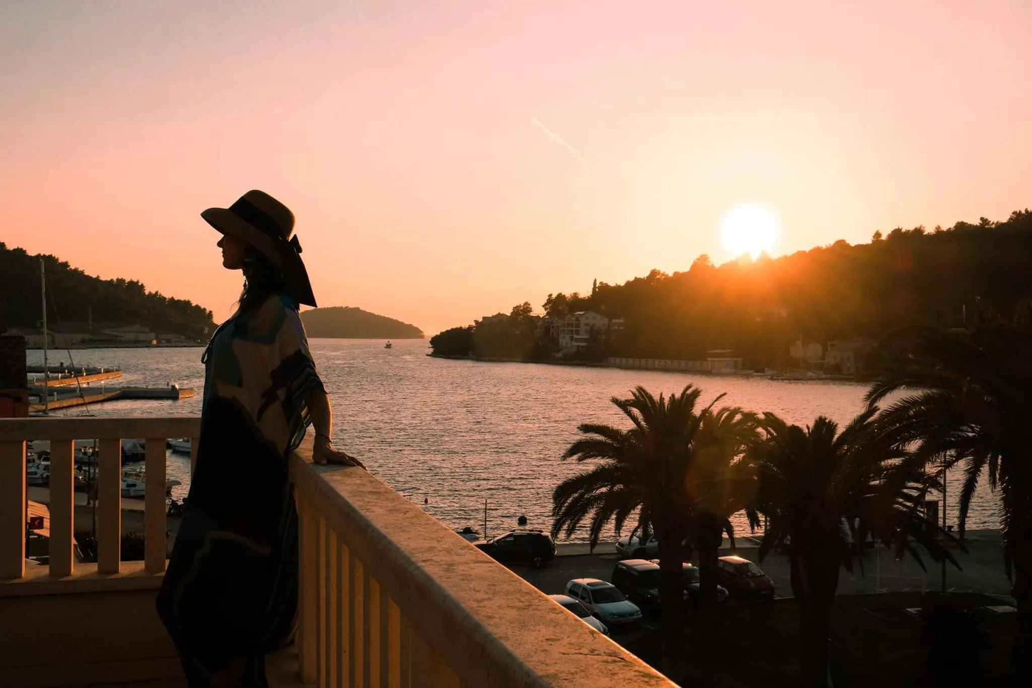 Une personne se tient sur une terrasse en admirant le coucher de soleil sur la mer.