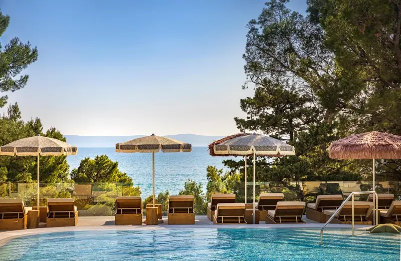 Transats et parasols ombragent une piscine bordée d'une terrasse en bois.