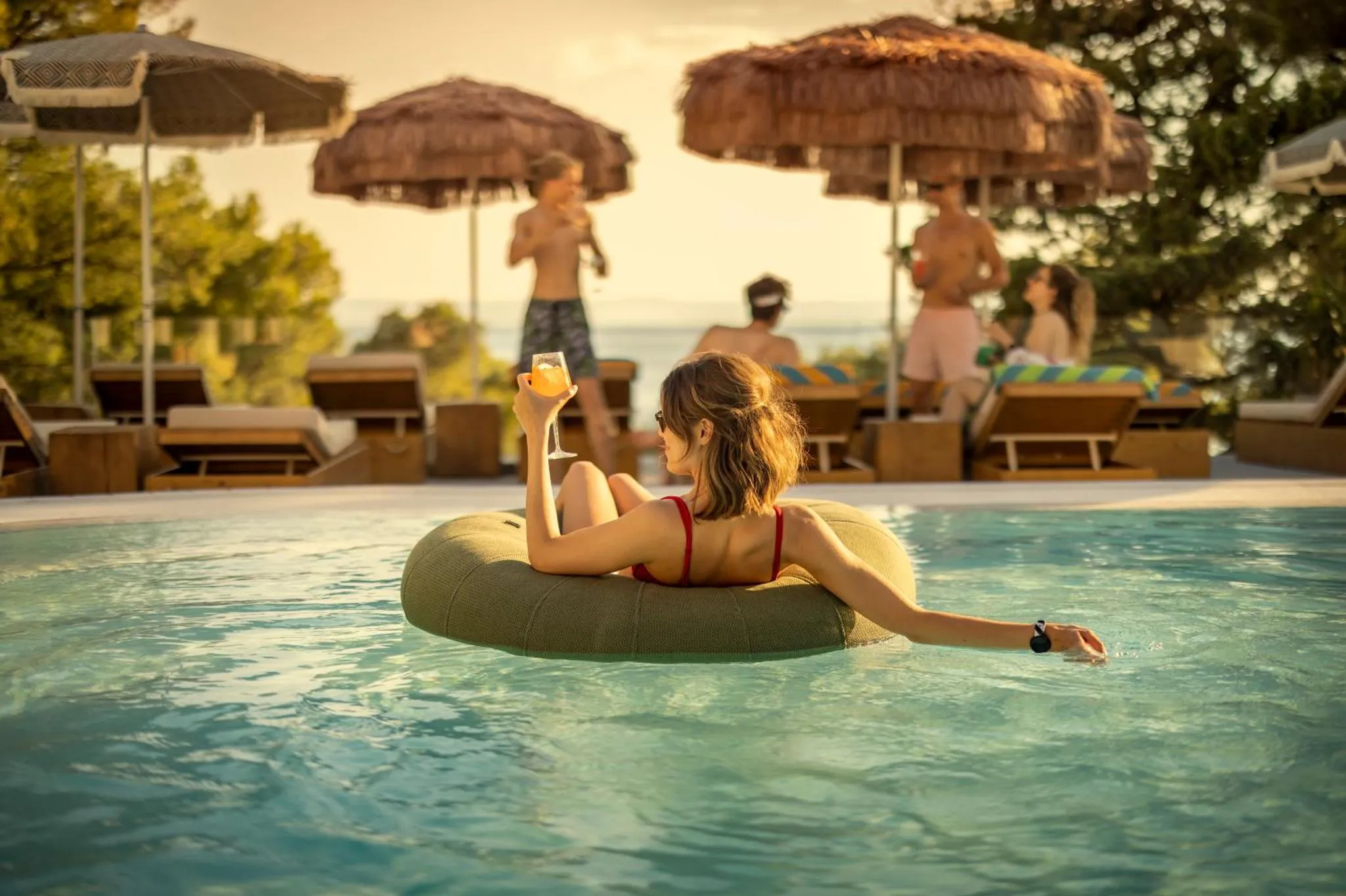 Une personne se détend dans une piscine avec un cocktail à la main.