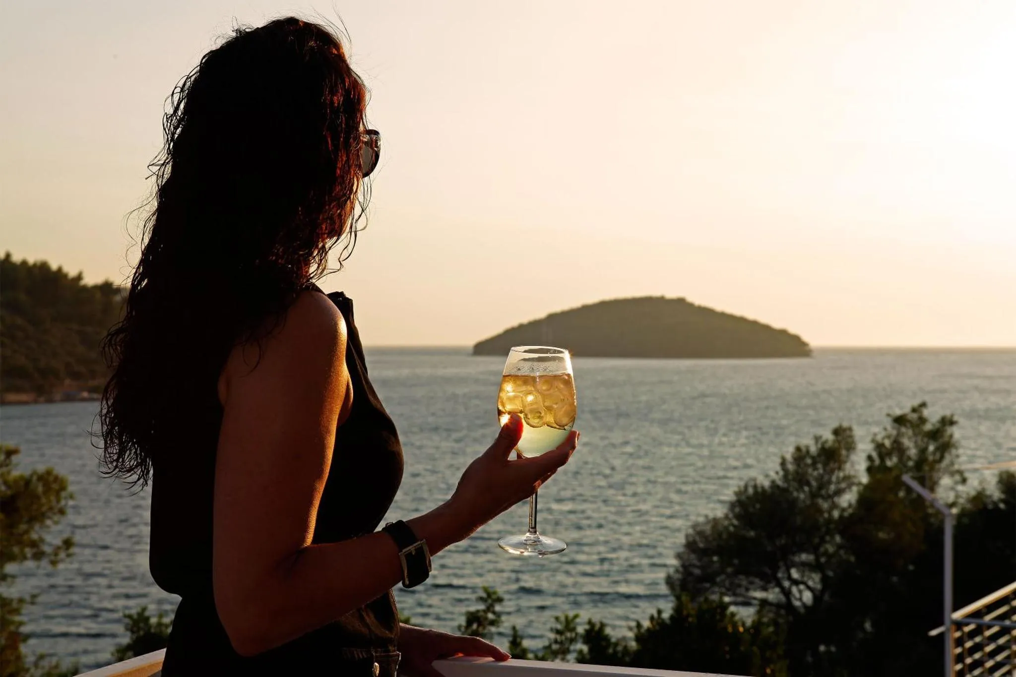Une personne admire la vue sur la mer en tenant un verre.
