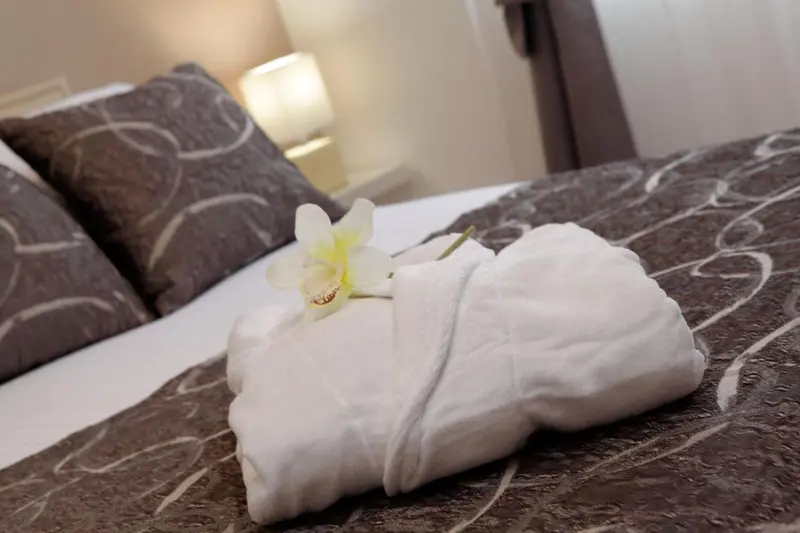 Un lit soigneusement fait est orné d'une fleur et d'une serviette pliée.