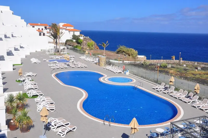 Vue aérienne d'une piscine d'hôtel avec des transats et la mer en arrière-plan.