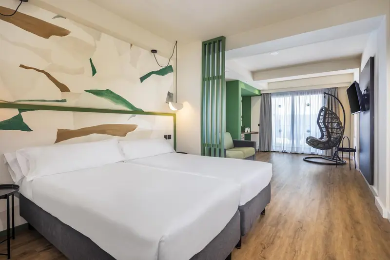 Chambre lumineuse avec un grand lit et un fauteuil suspendu.