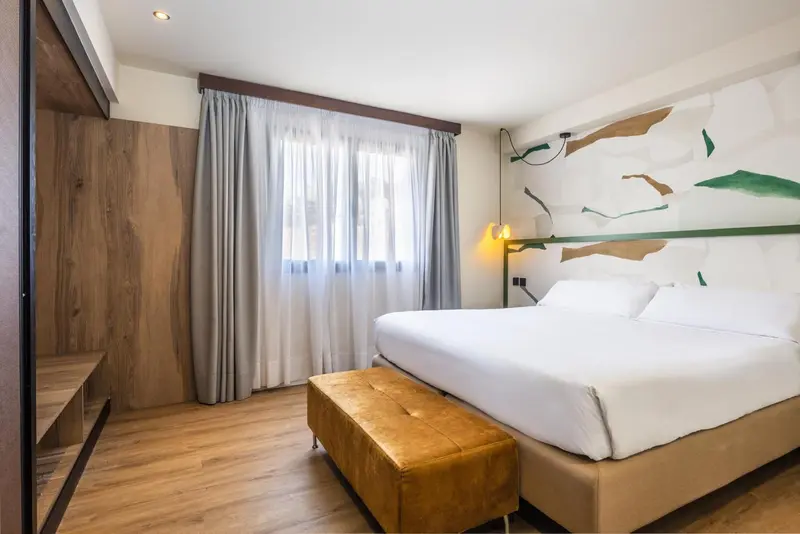 Une chambre lumineuse avec un grand lit et un décor mural abstrait.