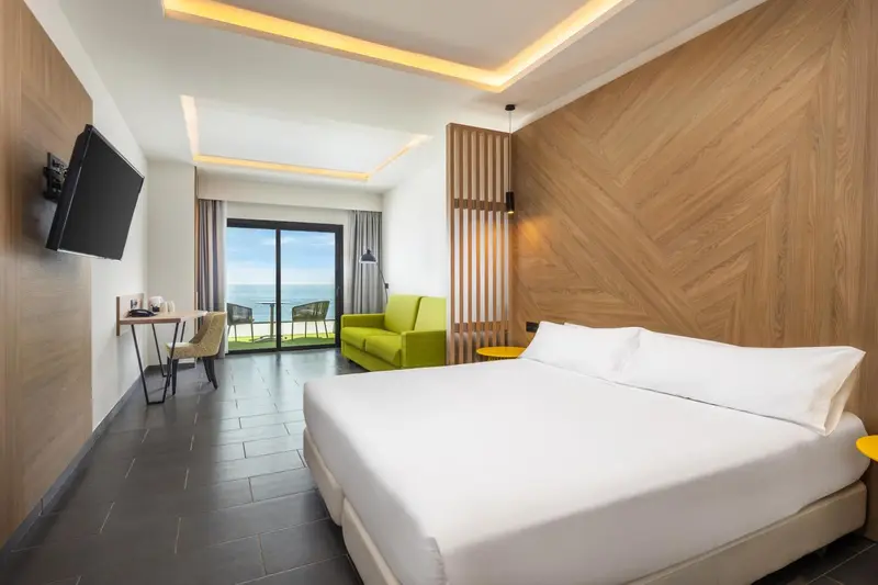 Une chambre lumineuse avec un lit et un espace salon donnant sur une vue mer.