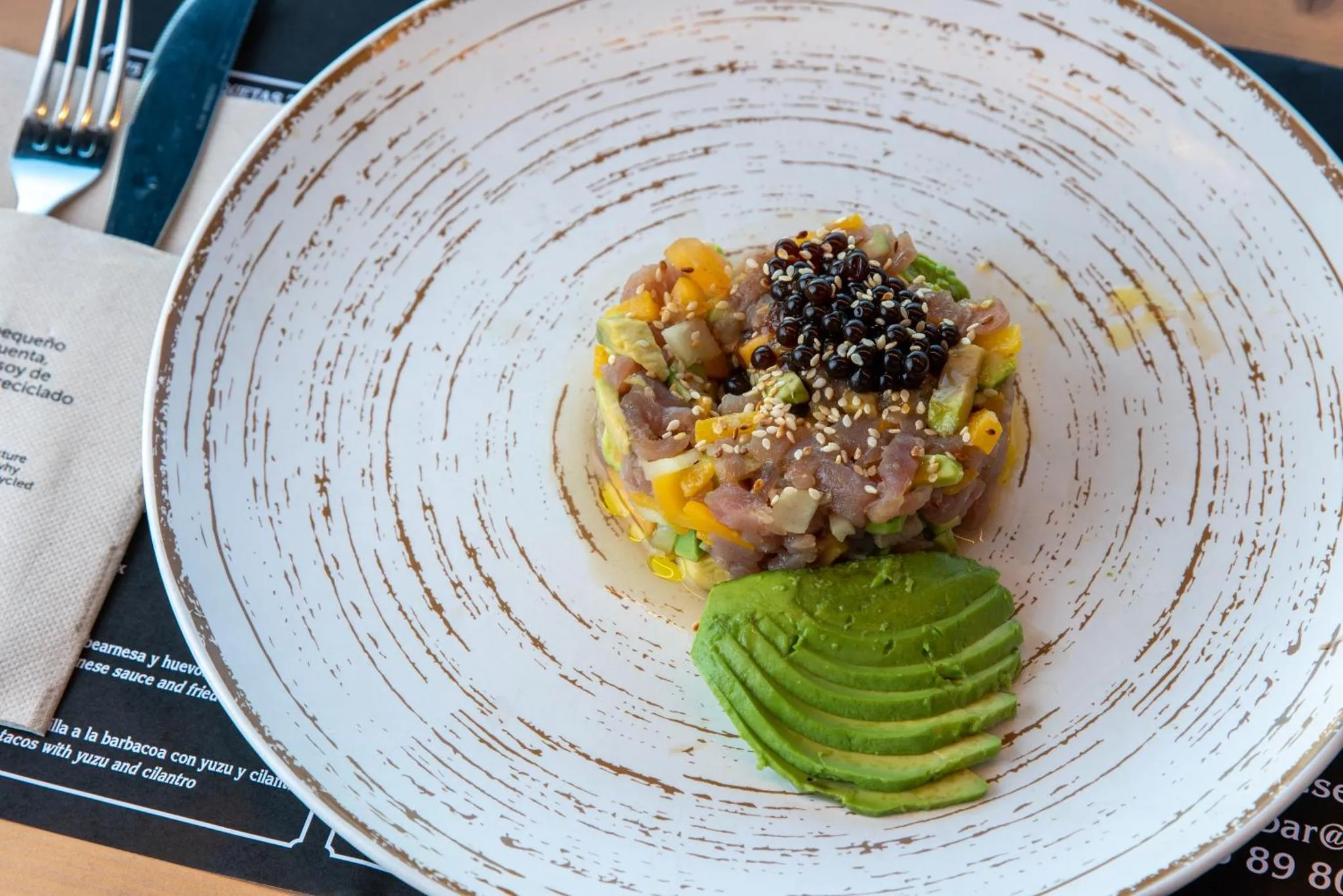 Assiette de poisson cru, avocat et sauce colorée sur une table.