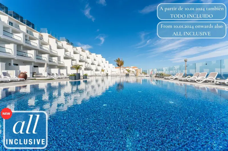 Vue d'une piscine turquoise devant un bâtiment blanc à plusieurs étages avec des transats.