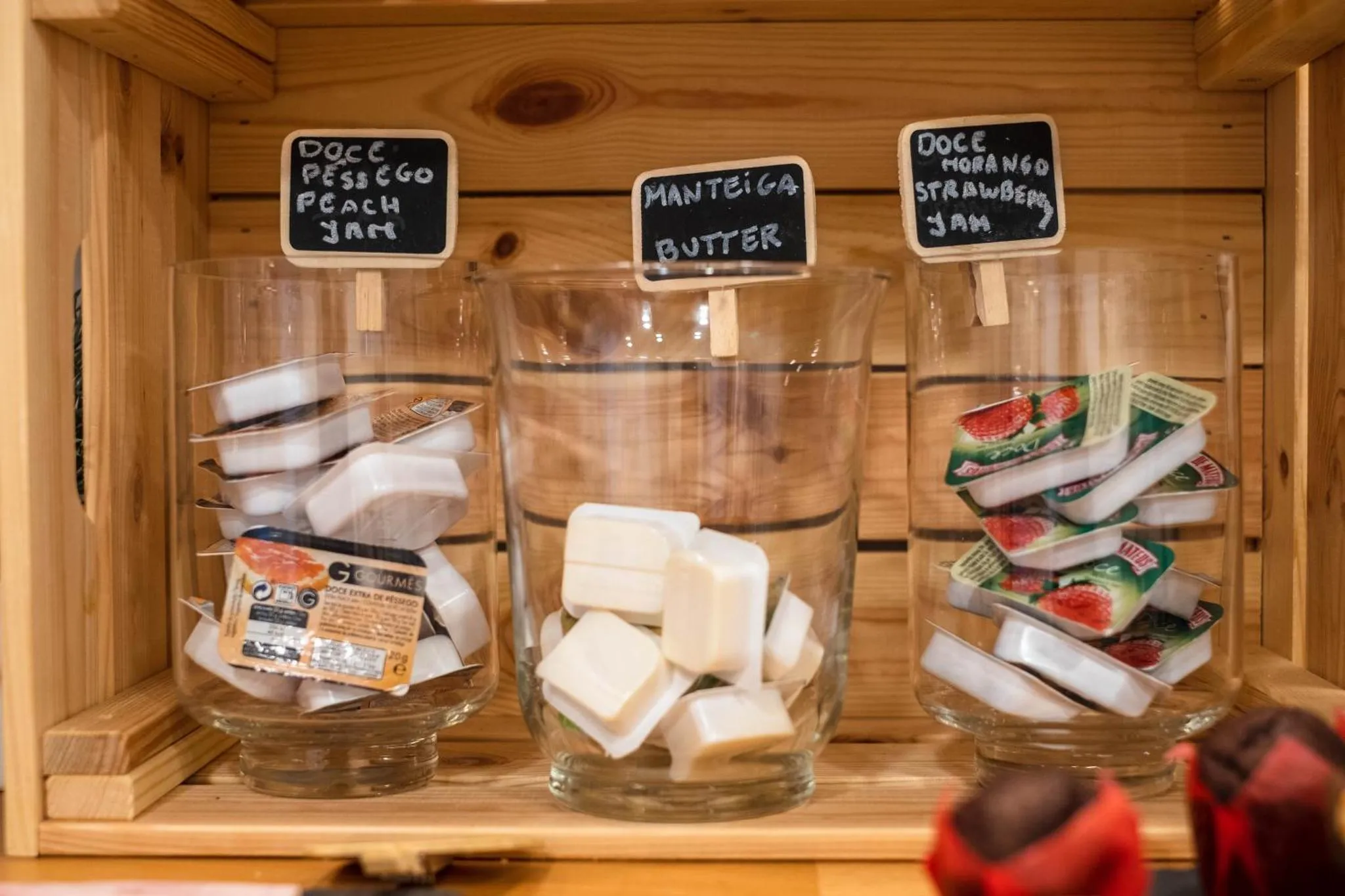 Des confitures et du beurre sont présentés dans des bocaux en verre sur une étagère en bois.