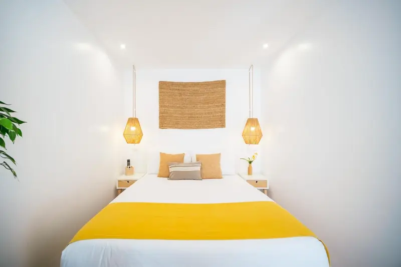 Une chambre lumineuse avec un grand lit recouvert d'une couverture jaune et de coussins.