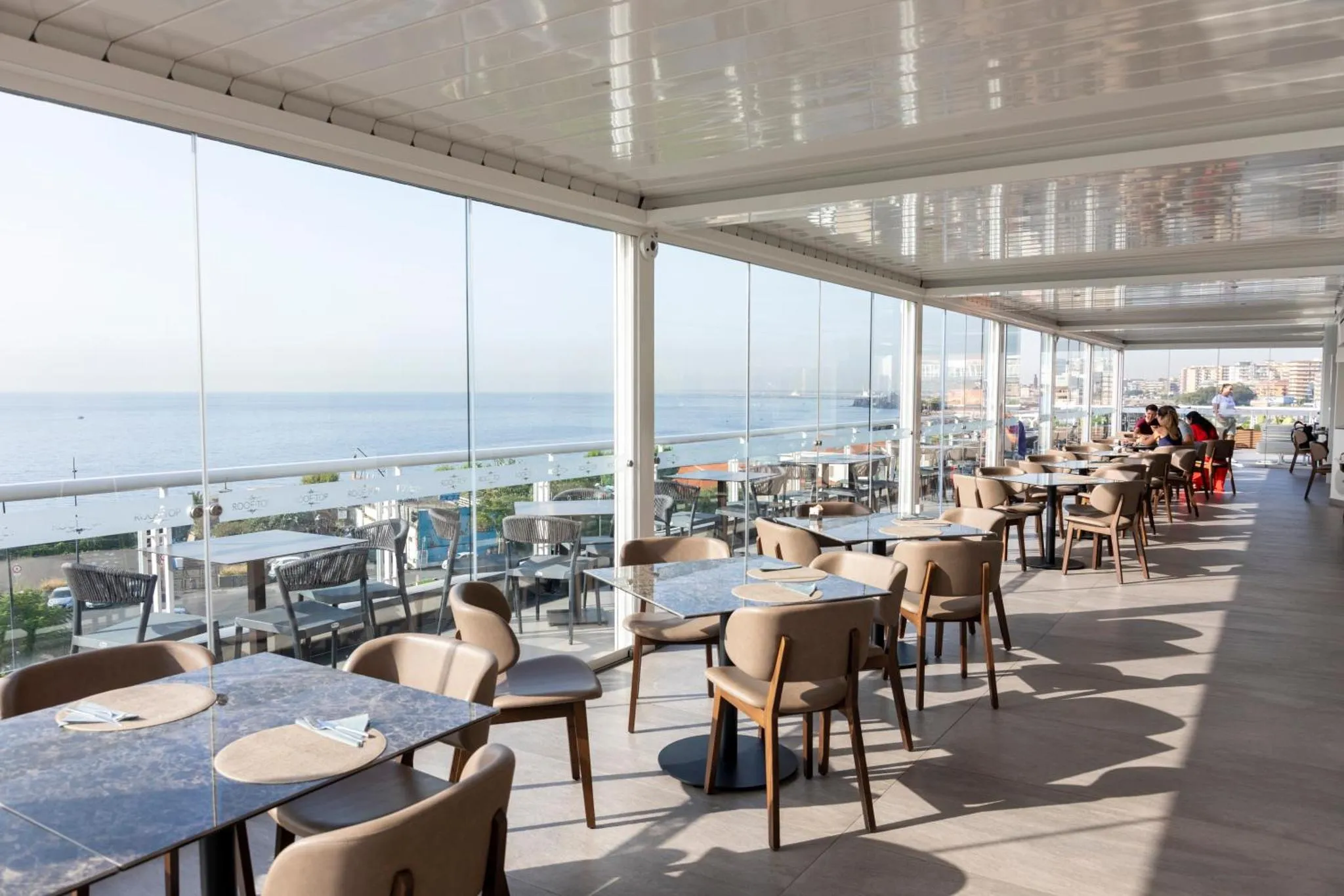 Terrasse ombragée avec tables et chaises donnant sur la mer.